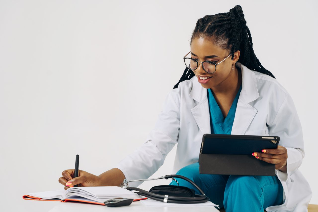 Services Smiling female doctor in scrubs using tablet and taking notes in a healthcare setting.