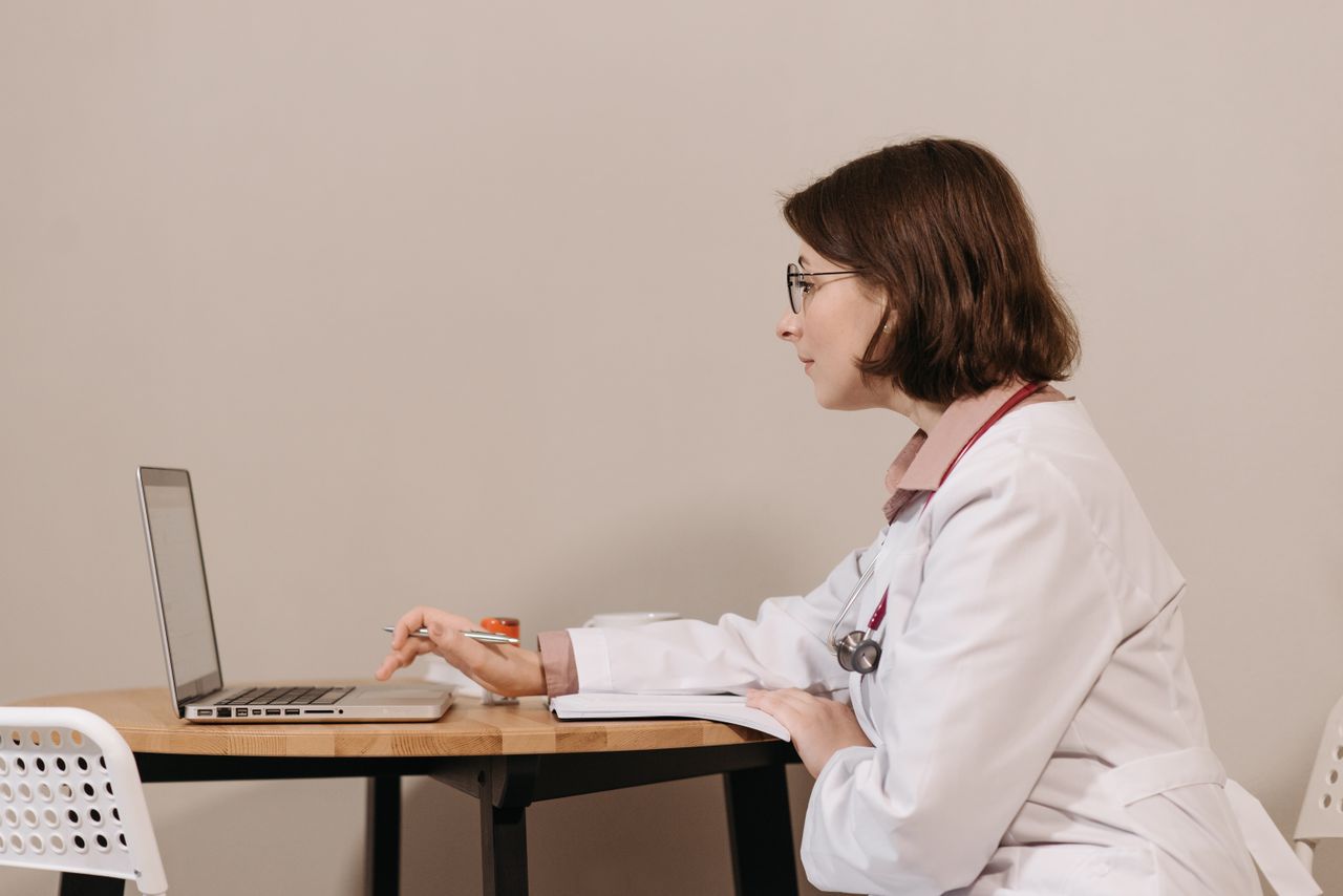 Services Side profile of a female doctor in a white coat working on a laptop at a desk.