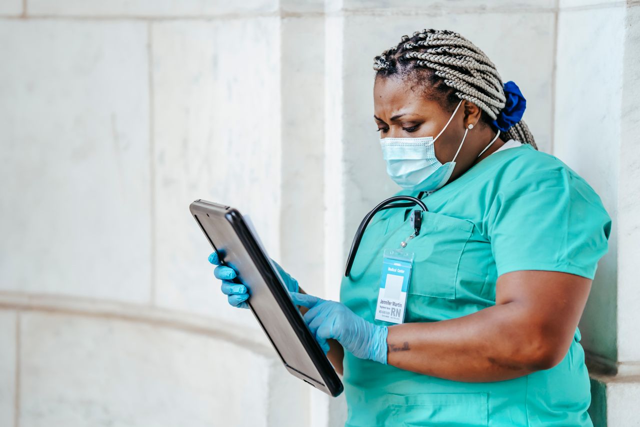 Services Focused middle aged ethnic female medic in uniform with clipboard and Afro braids in daylight
