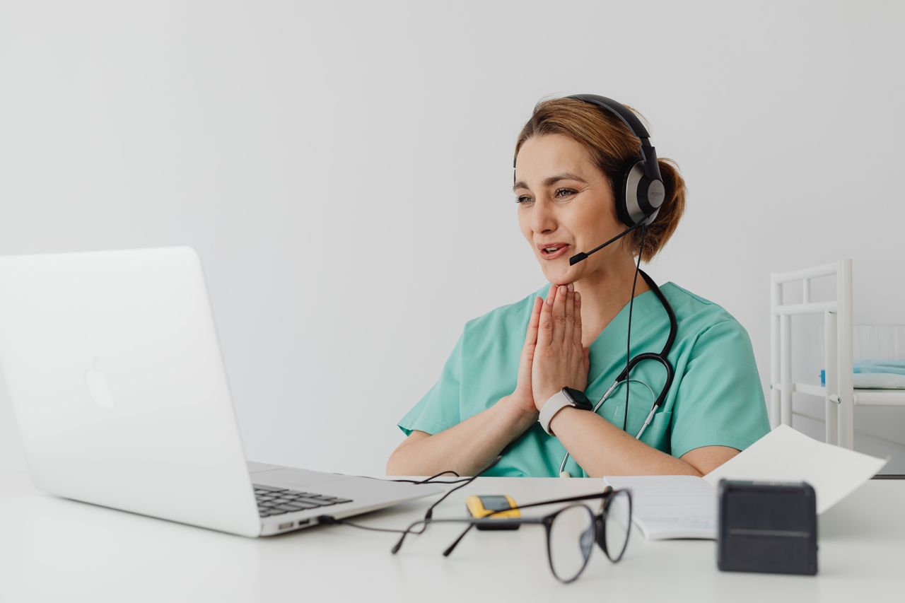 Services Female nurse using telemedicine for a virtual consultation on a laptop, wearing headphones and stethoscope.