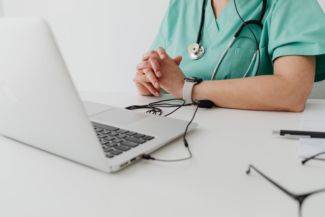 Services Medical practitioner in scrub suit using a laptop for remote consultation and documentation.